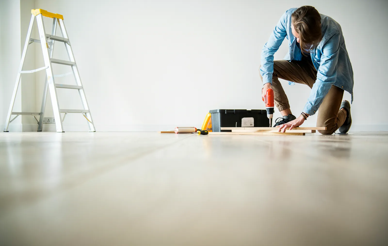 Handyman kneeling on a hardwood floor using a power drill during a home renovation
