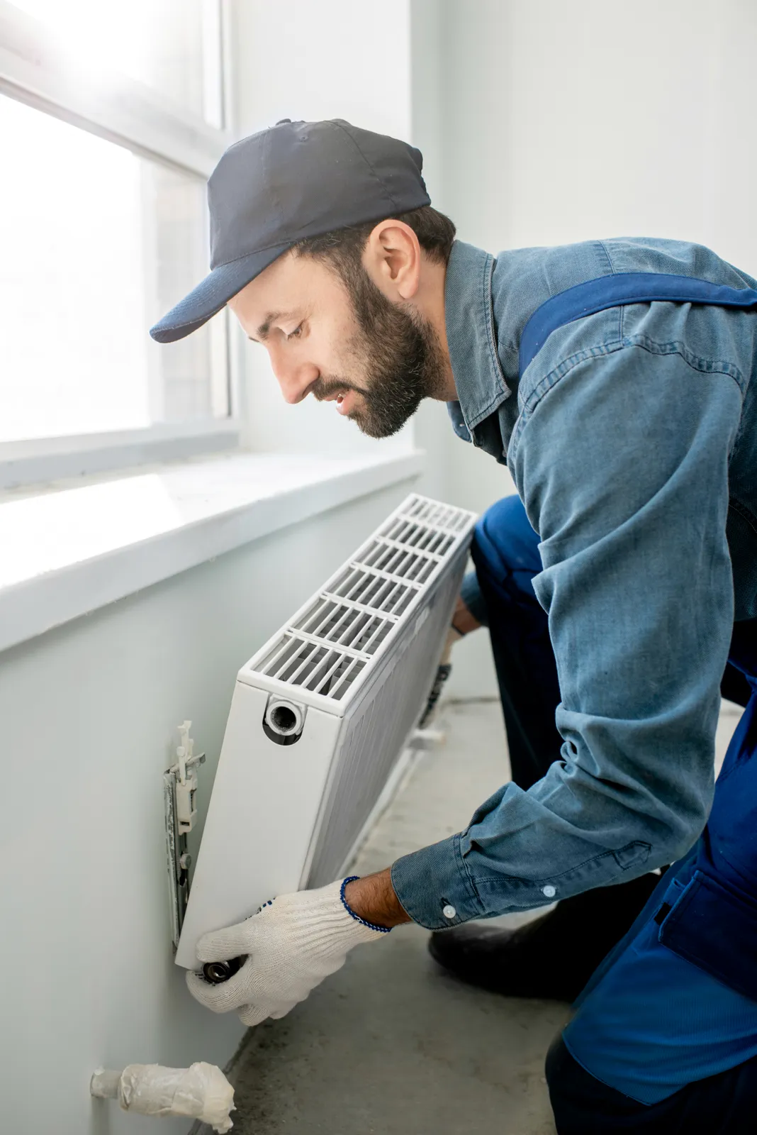 Tradesman fitting a radiator to a wall below a window